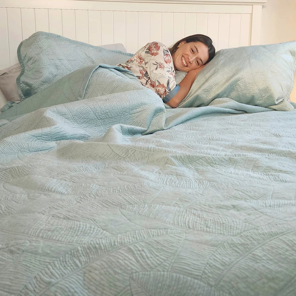 Woman lying in bed under a light blue comforter with a floral pillow.