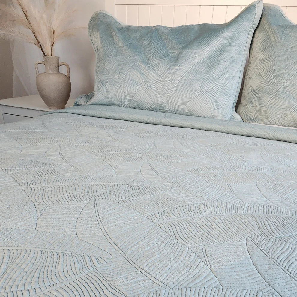 Textured light blue bedding set on a bed with a vase in the background.