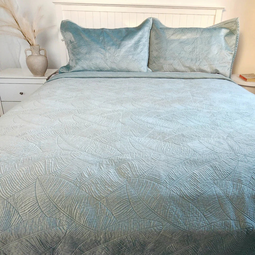 Blue textured bedspread on a bed with matching pillows in a bedroom setting.