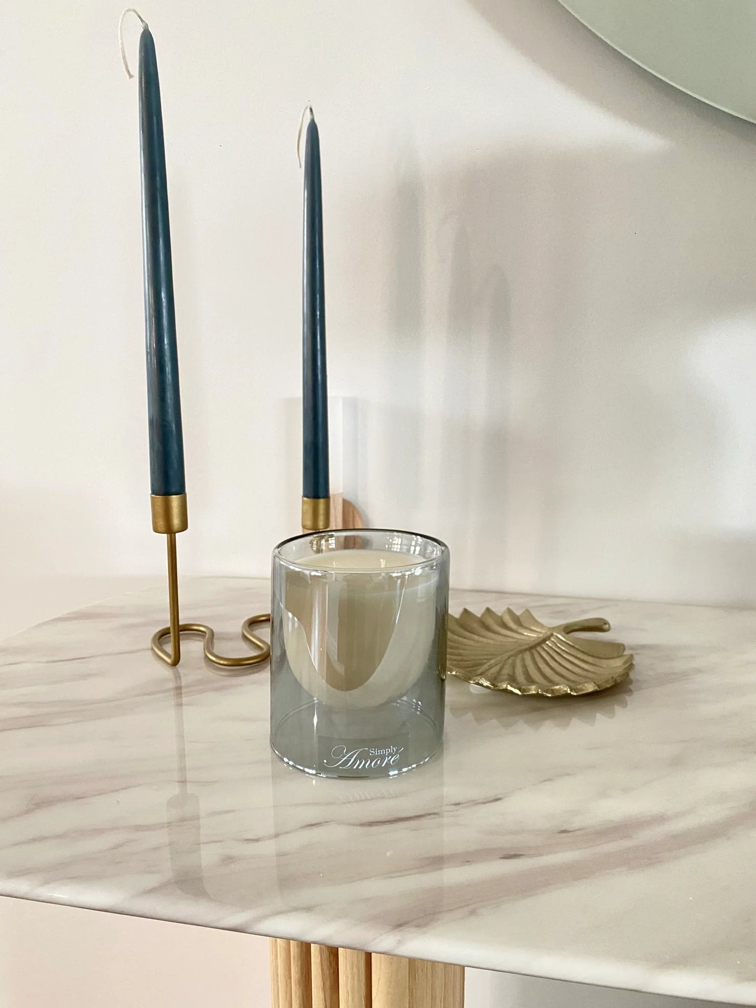 Glass candle holder with a candle on a marble surface, flanked by two blue candles in holders.
