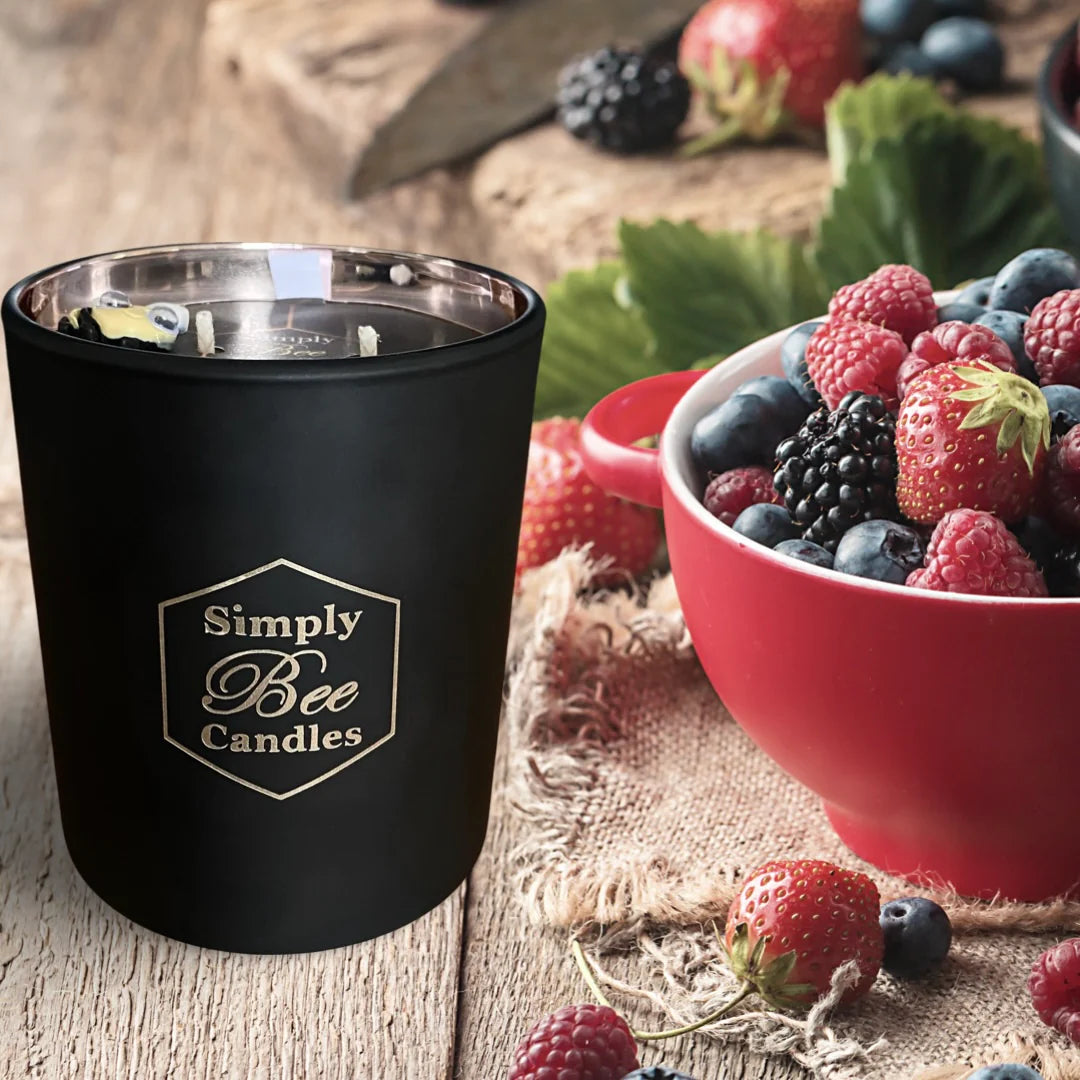 Black candle with 'Simply Bee Candles' logo on a wooden surface with berries.