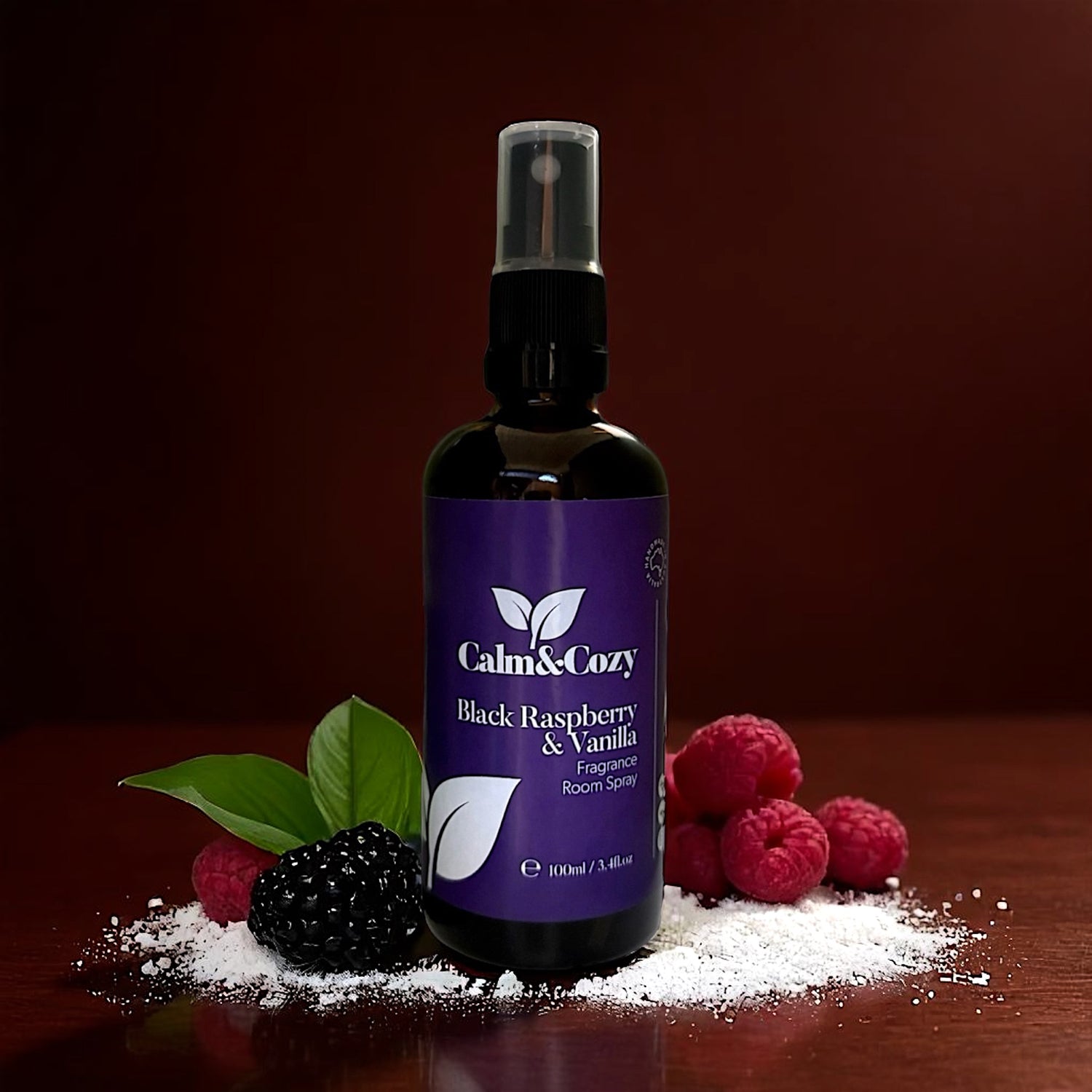Bottle of Calm & Cozy Black Raspberry & Vanilla room spray with berries on a wooden surface.
