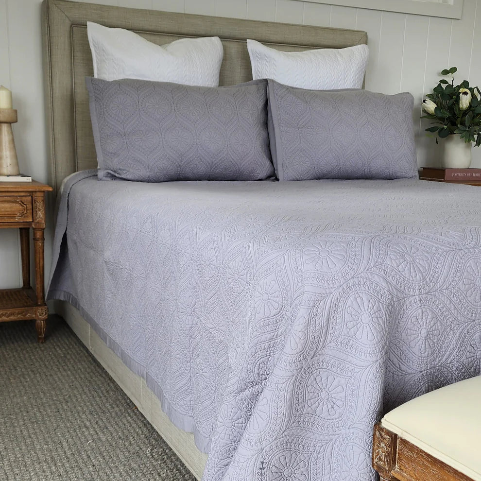Bed with gray patterned bedding and pillows in a bedroom setting.