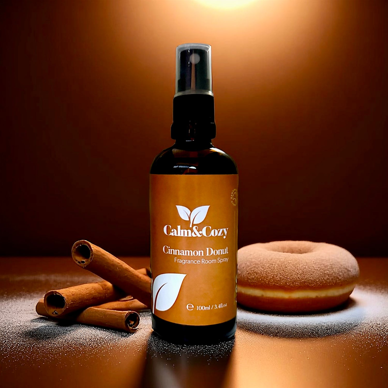 Fragrance room spray bottle labeled 'Calm & Cozy Cinnamon Donut' with cinnamon sticks and a donut on a brown background.