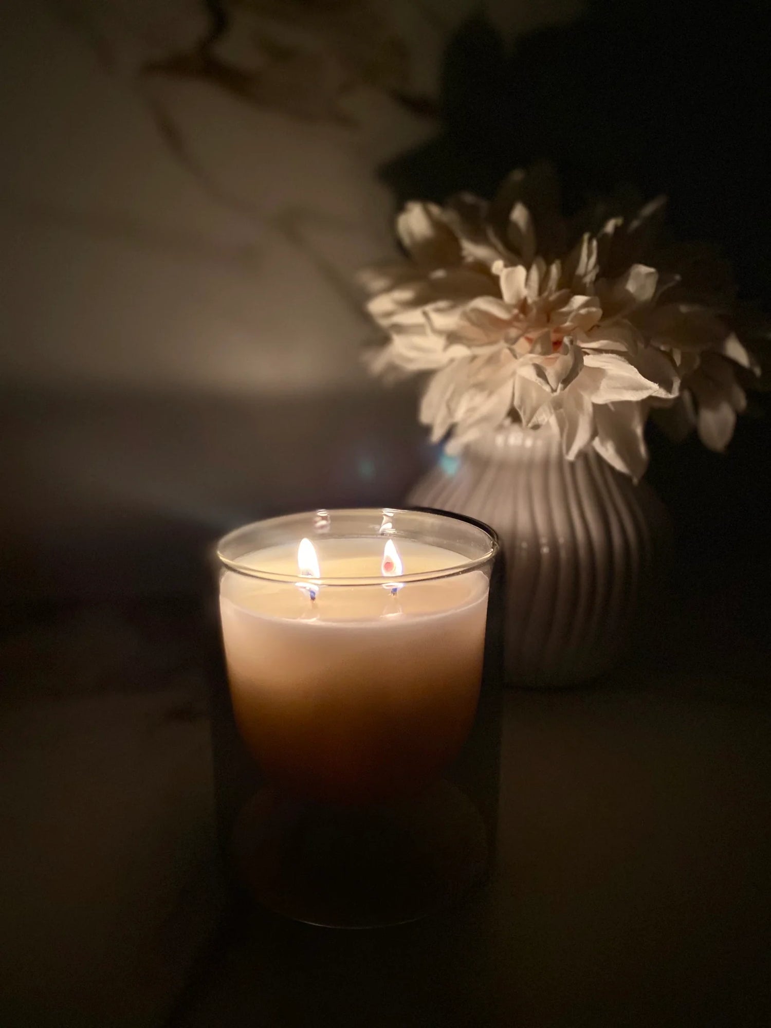Candle with two flames next to a vase with flowers in a dimly lit setting