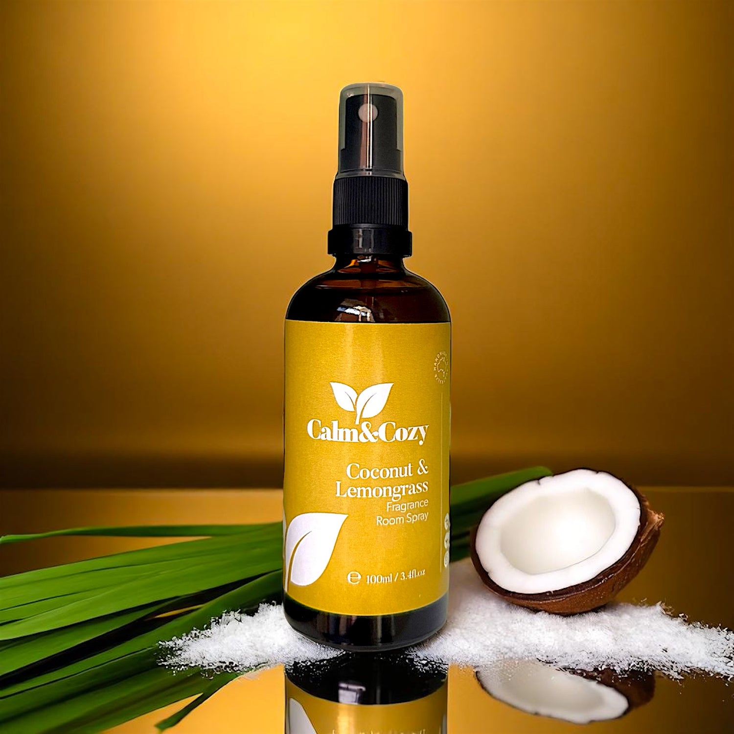 Bottle of Calm & Cozy coconut and lemongrass product with a yellow label, surrounded by coconut pieces and leaves on a reflective surface.