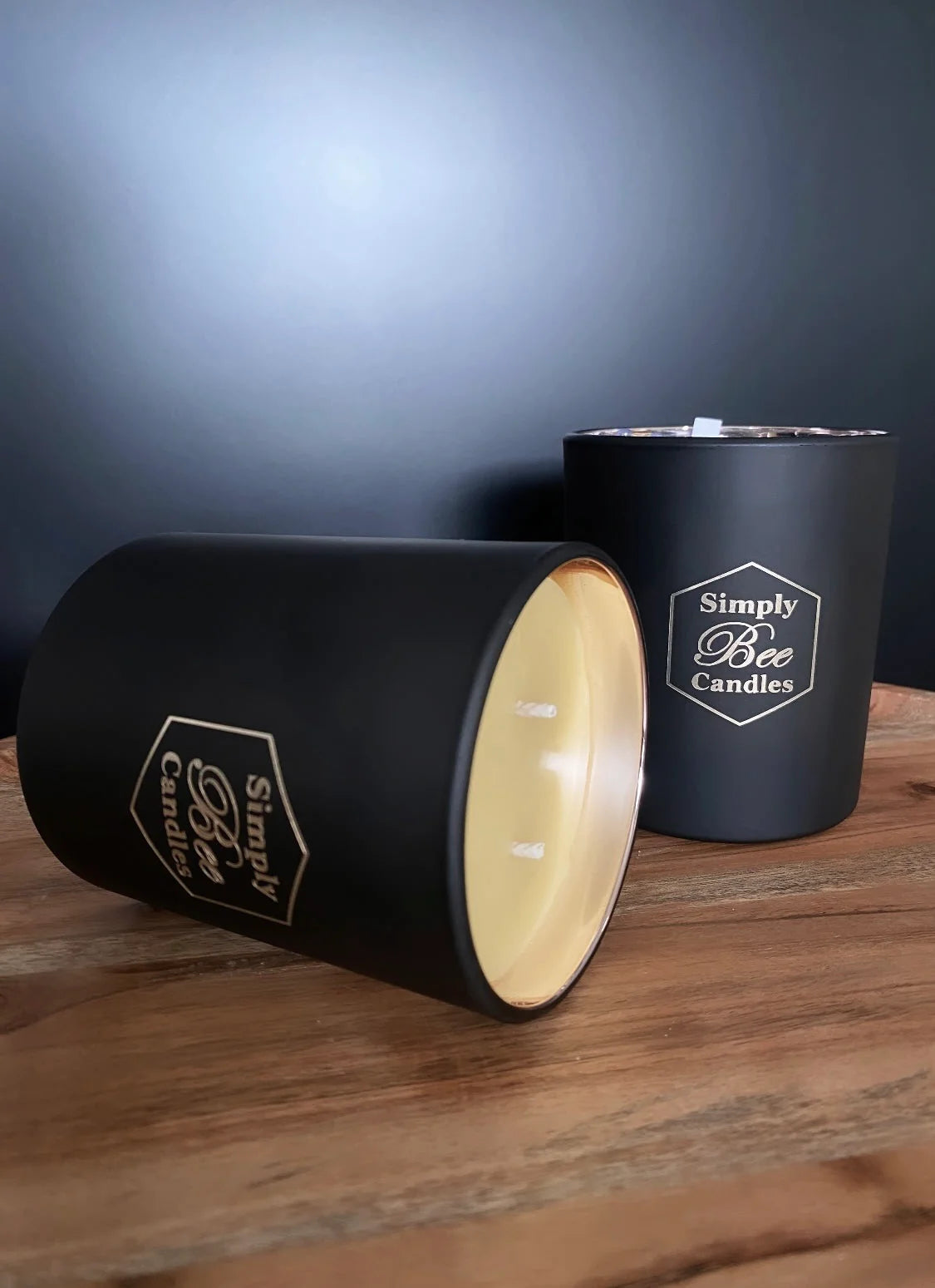 Two black candles with 'Simply Bee Candles' branding on a wooden surface.