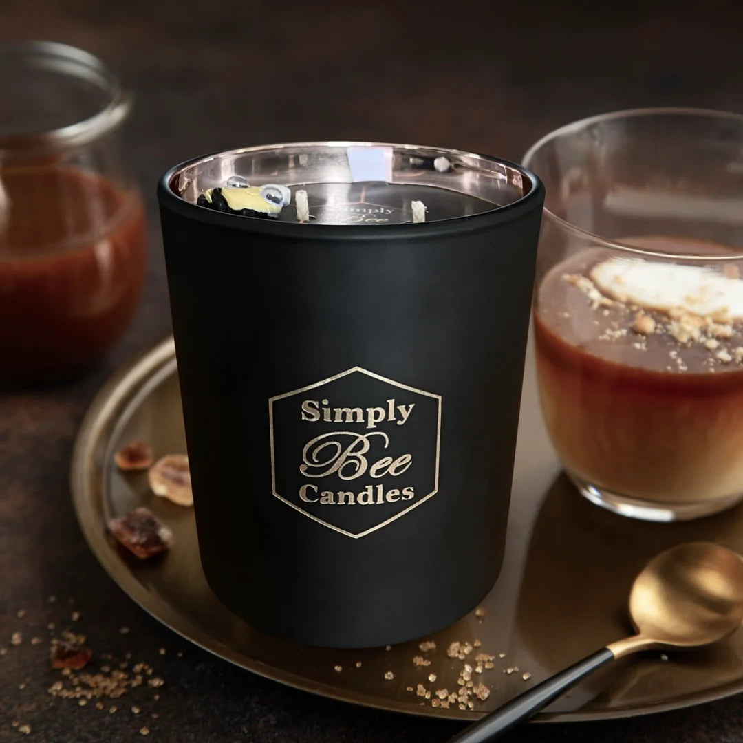 Black candle with 'Simply Bee Candles' logo on a dark surface with a spoon and dessert.