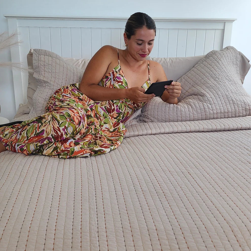 Woman in a colorful dress sitting on a bed using a phone.