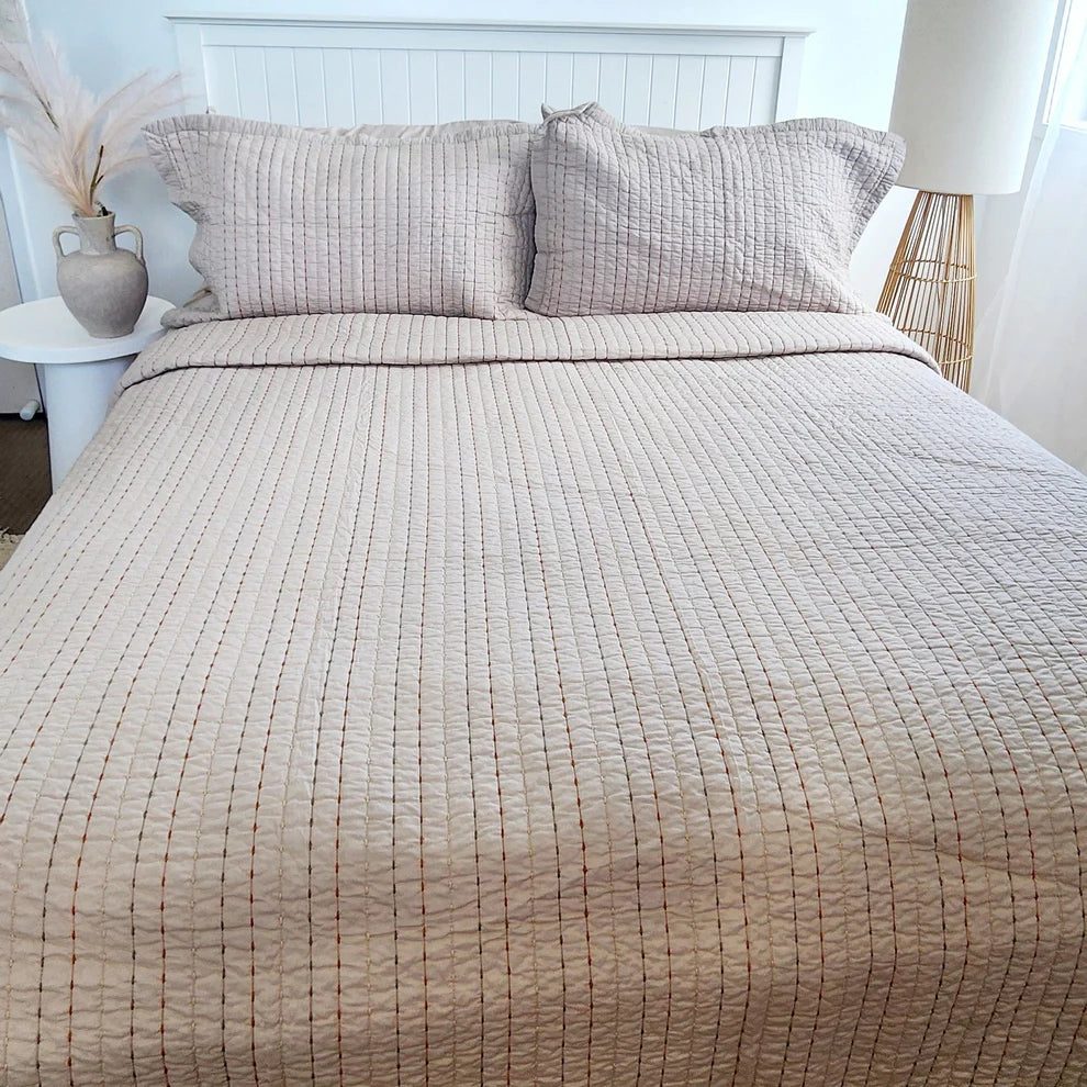 Neatly made bed with textured beige bedding and matching pillows in a bedroom setting.