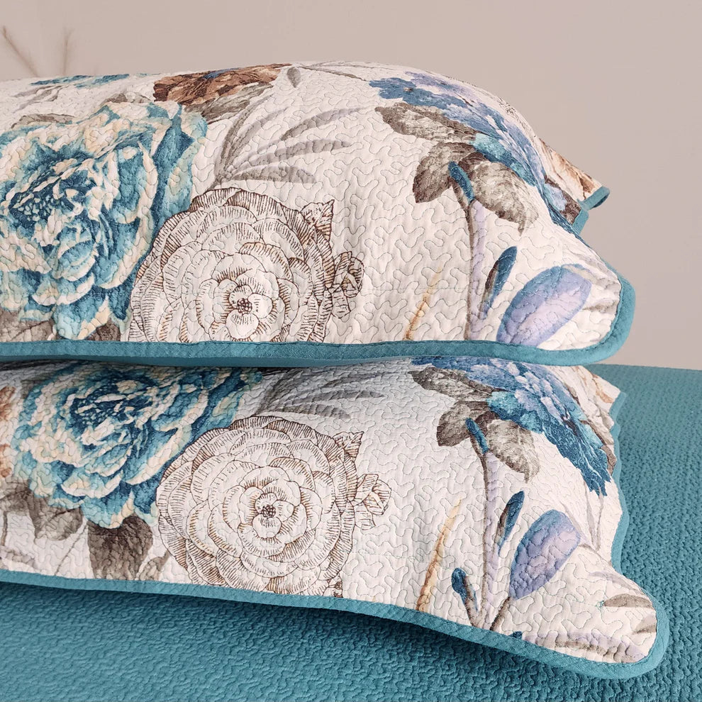 Floral patterned quilt with blue and beige colors on a teal bedspread.