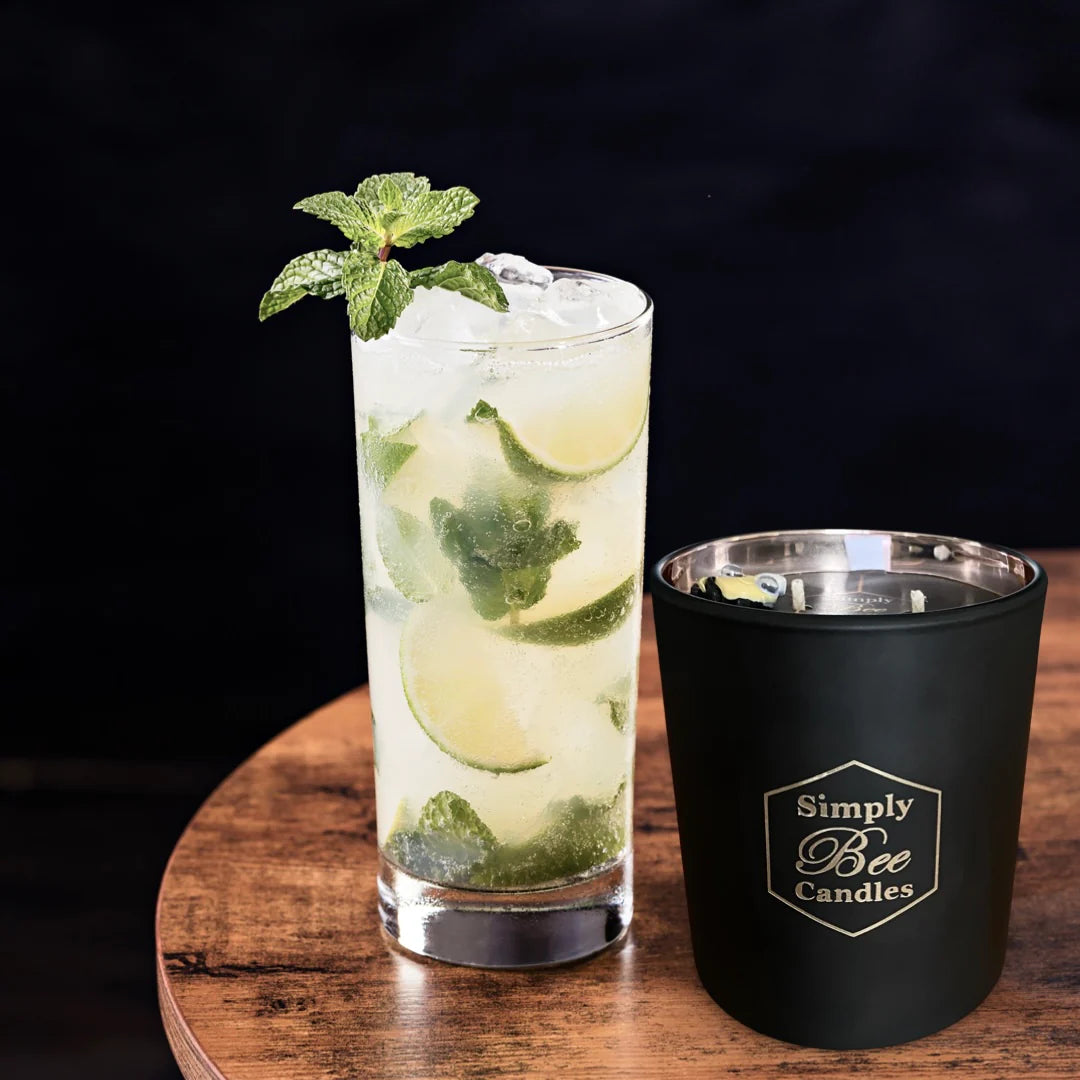Glass of iced drink with lime and mint next to a black container labeled 'Simply Bee Candles' on a wooden surface.