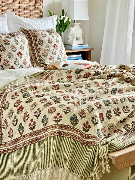 Decorative floral quilt on a bed with pillows and a lamp in the background