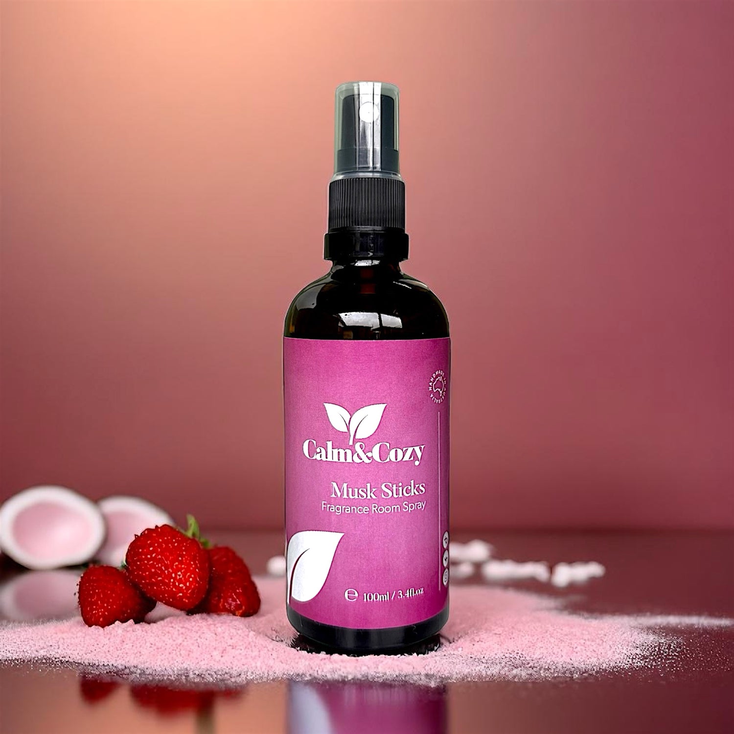 Bottle of Calm & Cozy Musk Sticks perfume on a pink surface with strawberries.