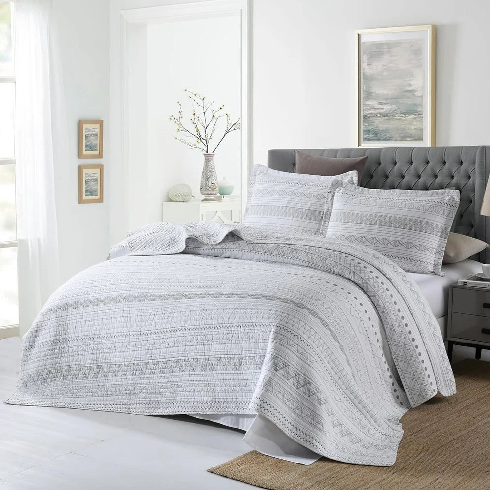 Gray quilt set on a bed in a bedroom with white walls and framed art.