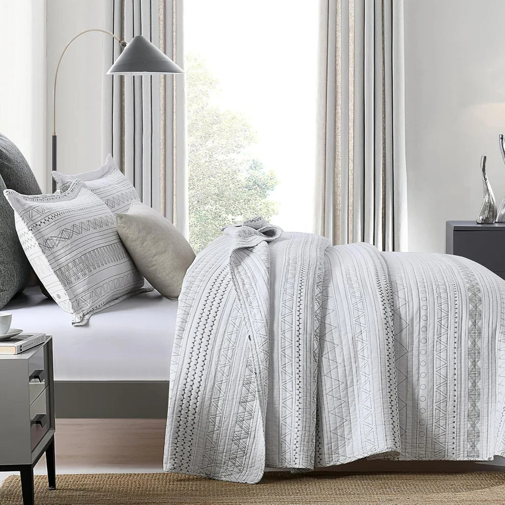 Bedroom with a bed covered in a patterned gray and white comforter, pillows, and nightstands.