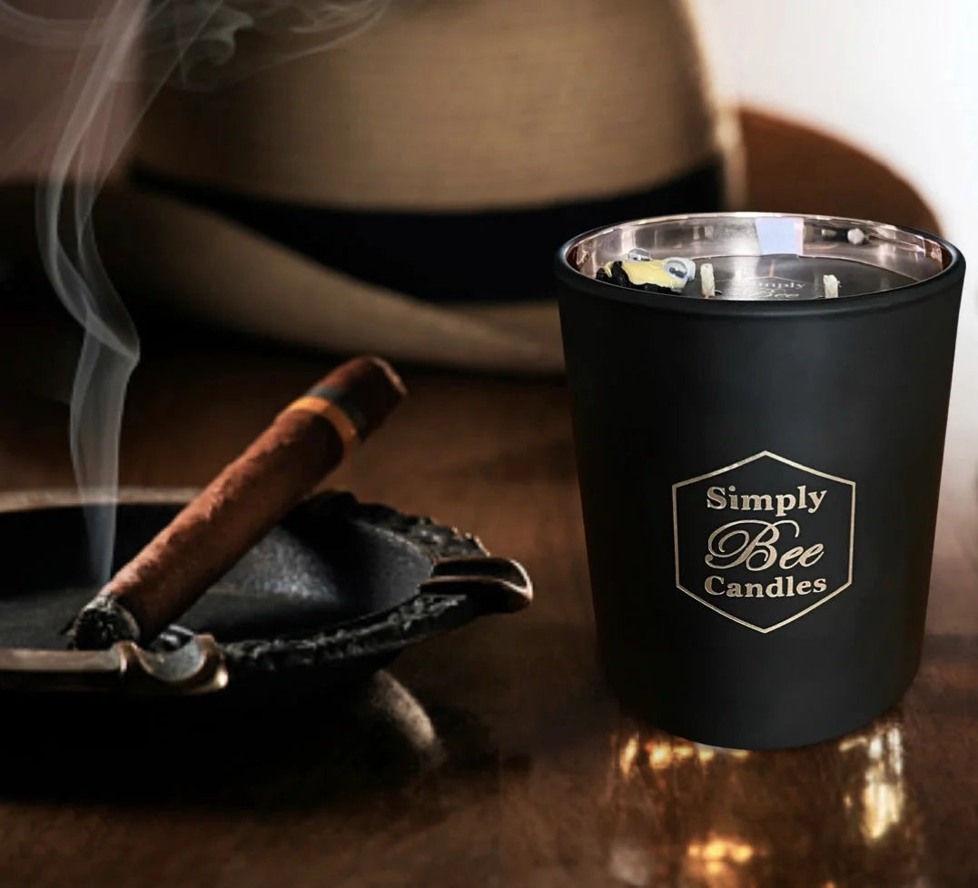 Black candle holder with 'Simply Bee Candles' logo next to a smoking cigar on a wooden surface.