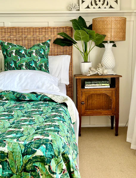 Bedroom with wicker headboard, green leaf-patterned bedding, and wooden nightstand.