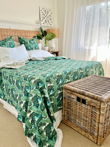 Bedroom with a bed covered in a green leaf-patterned comforter, wicker basket, and decorative pillows.
