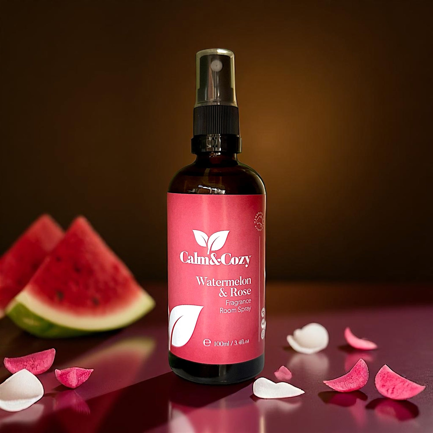 Bottle of Calm & Cozy Watermelon & Rose floral spray with watermelon slices and petals on a dark background