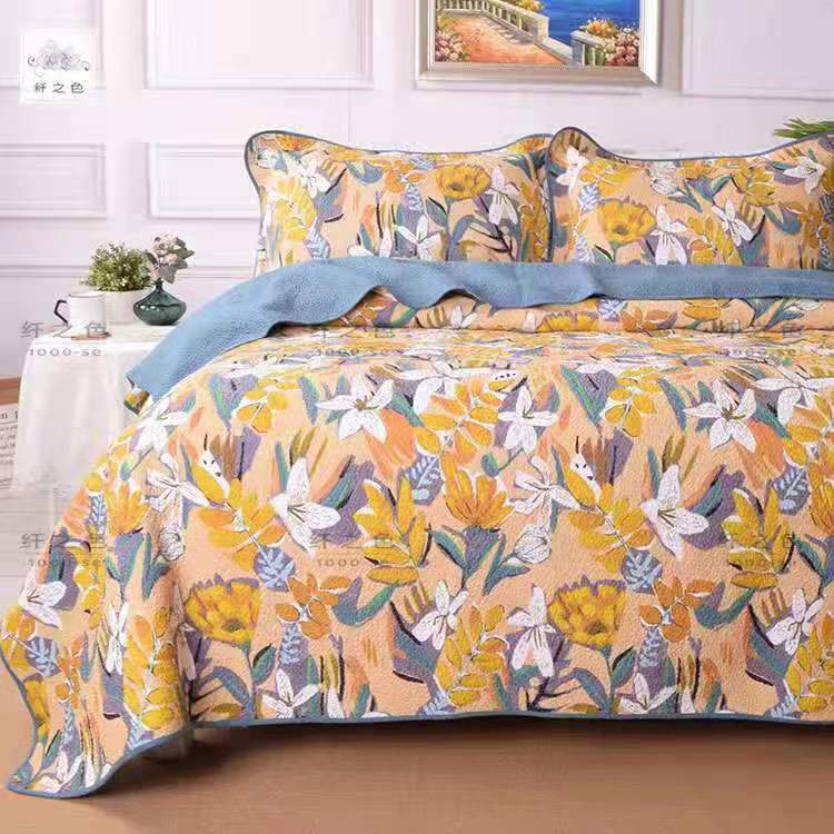Floral patterned bedspread set on a bed with a decorative pillow in a bedroom setting.