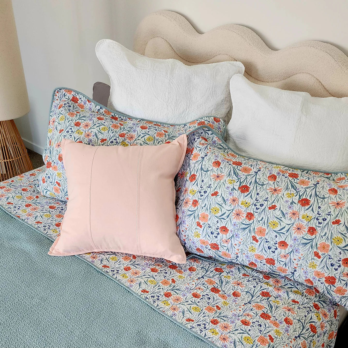 Floral bedding with a pink pillow on a bed with a wavy headboard.