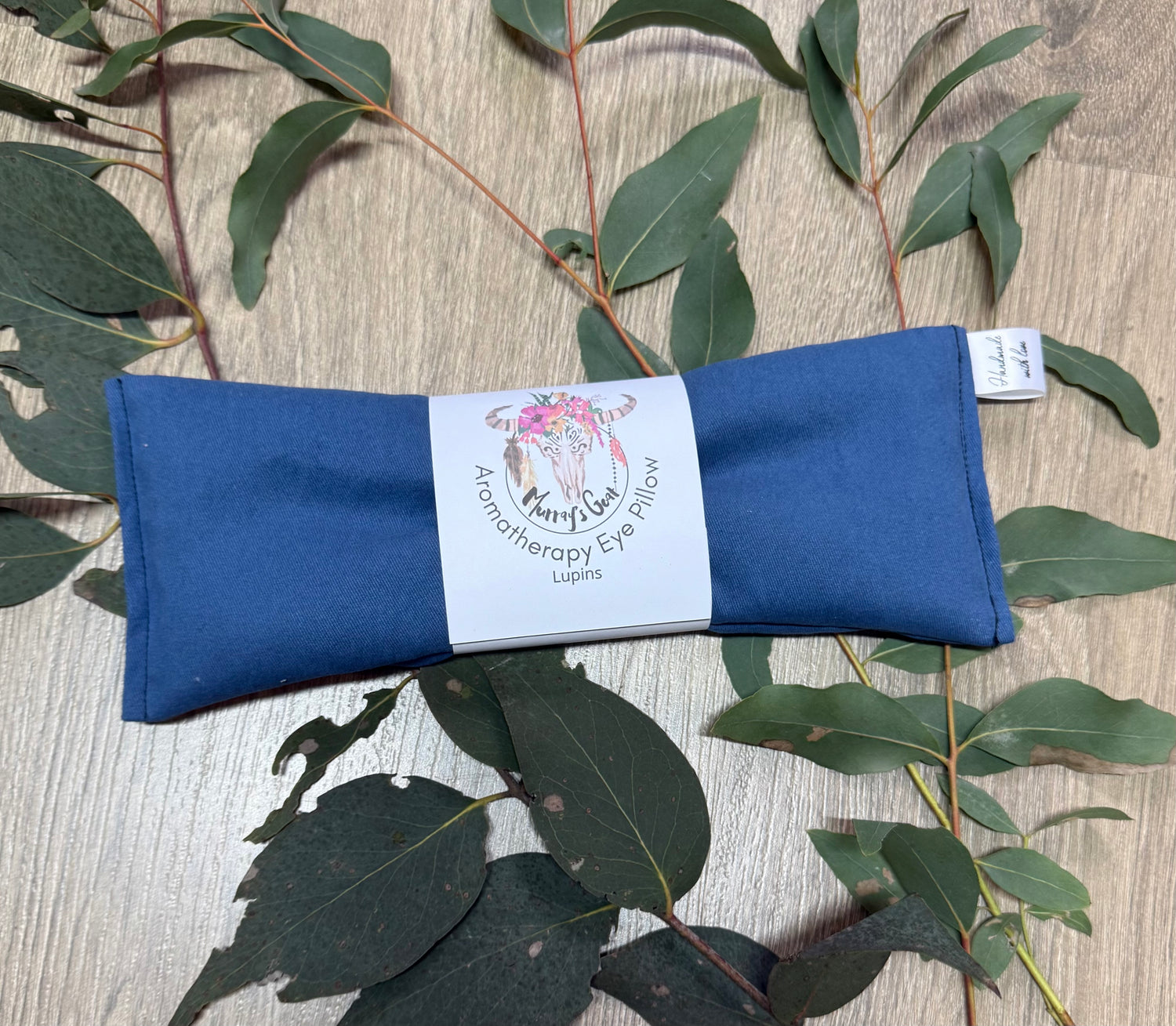 Blue eye pillow with a label on a wooden surface with eucalyptus leaves