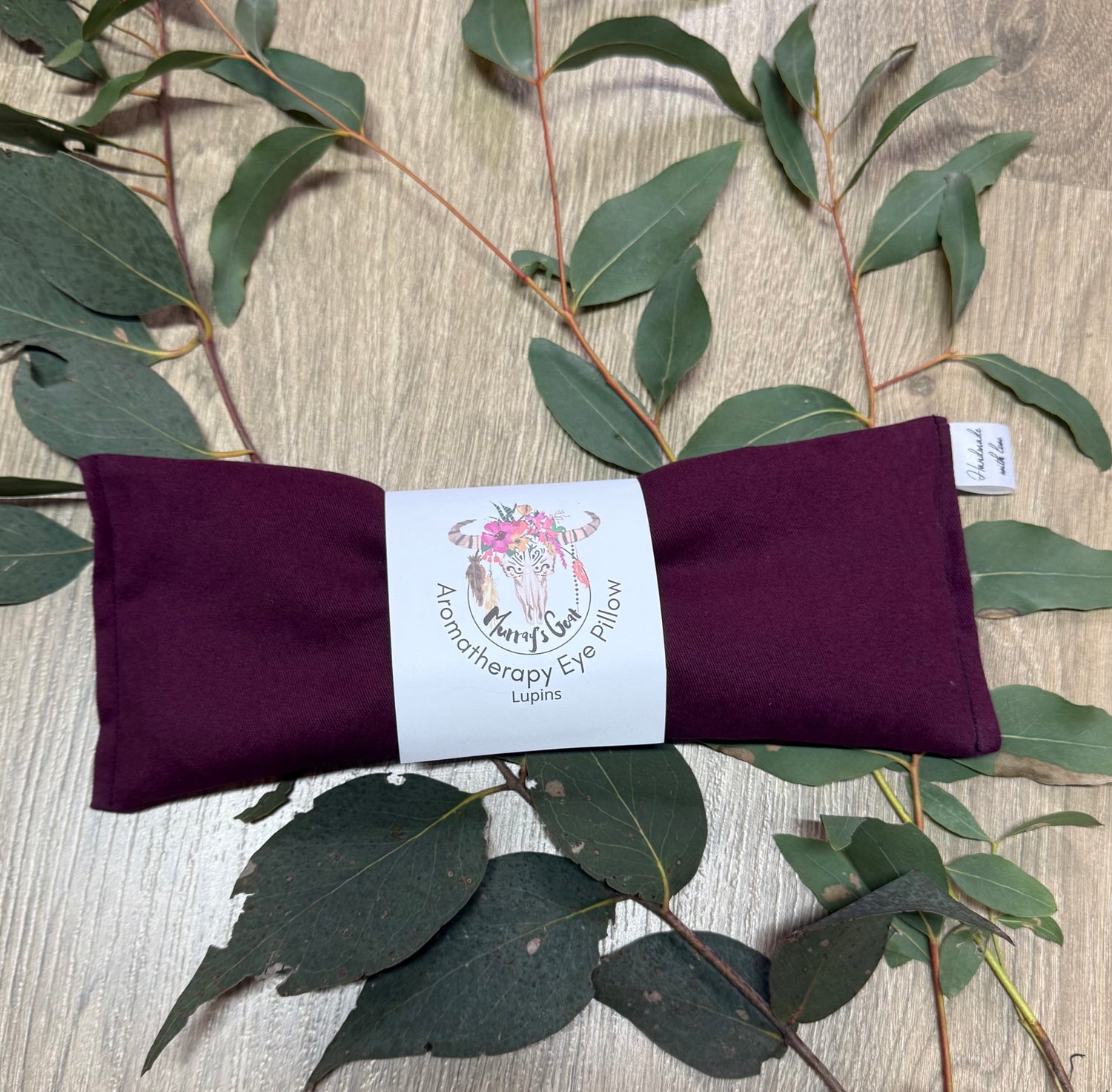 Purple eye pillow with a label on a wooden surface with eucalyptus leaves