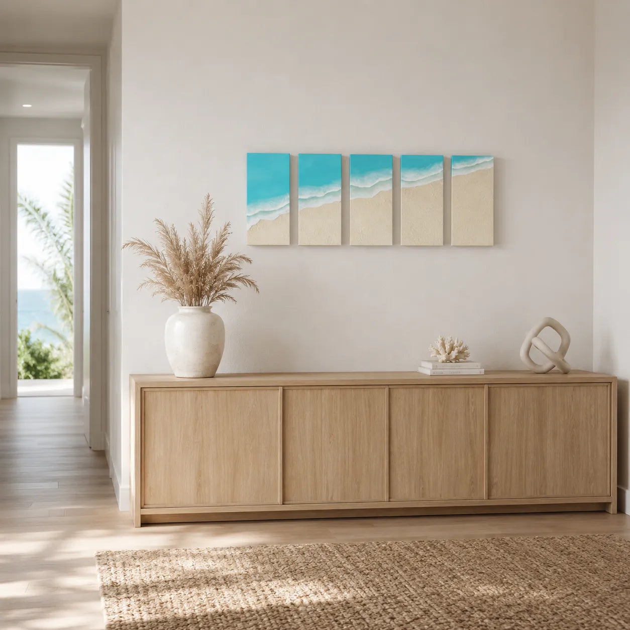 A 4-panel canvas wall art set depicting a turquoise ocean and beige beach, displayed in a modern living room setting above a light wood credenza.