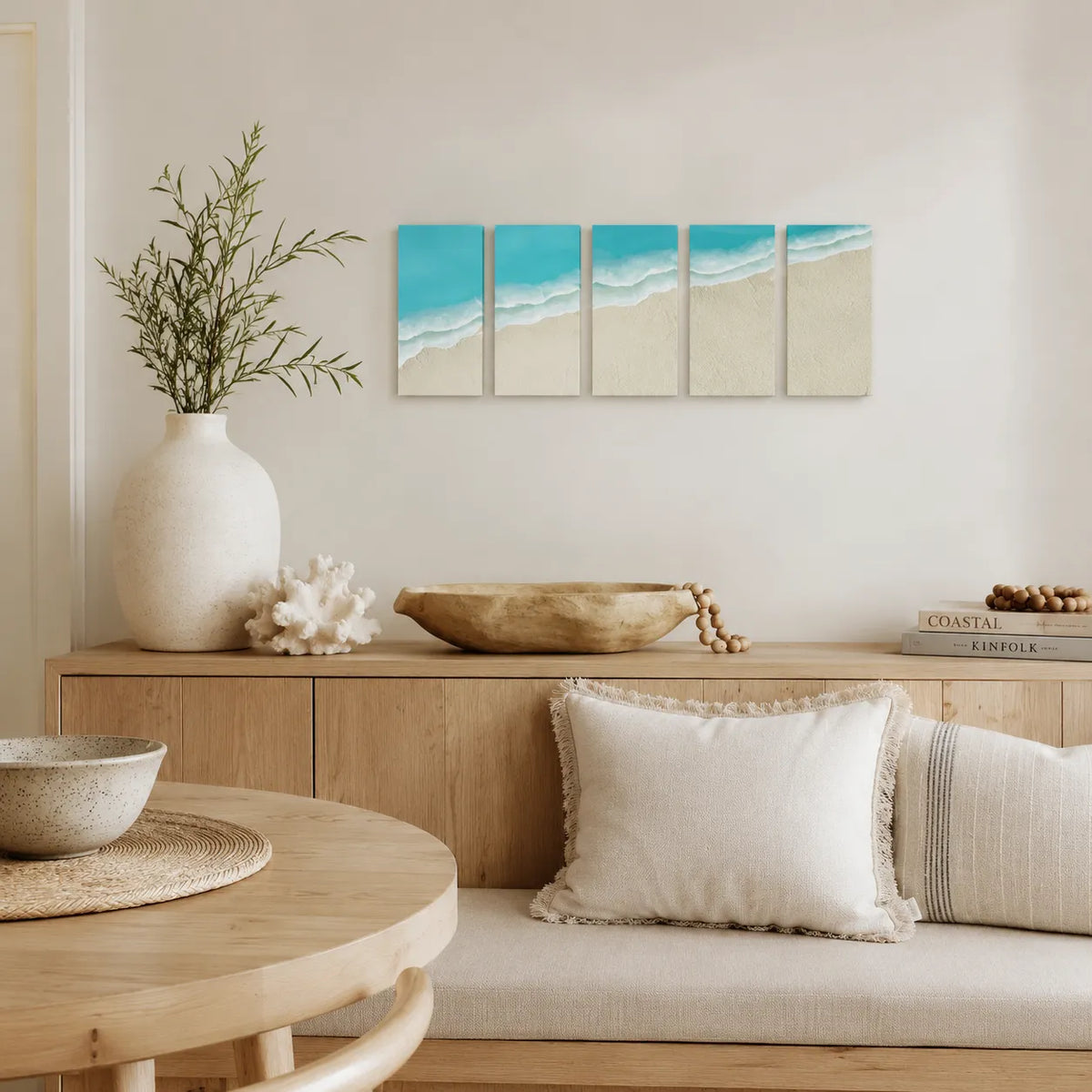 A five-panel canvas wall art set depicting turquoise ocean waves rolling onto a sandy beach, displayed in a modern, minimalist living room setting above a wooden console table.