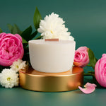 White candle on a gold stand with pink and white flowers on a green background