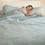 Woman lying in bed under a light blue comforter with a floral pillow.