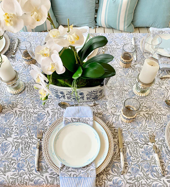 Elegant table setting with white orchids, patterned tablecloth, and decorative plates.