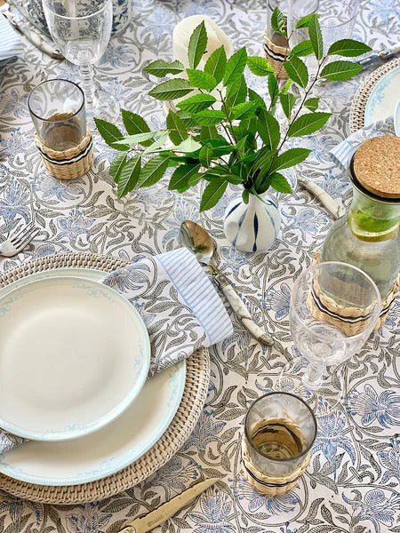Elegant table setting with plates, glasses, and a vase of greenery on a patterned tablecloth.
