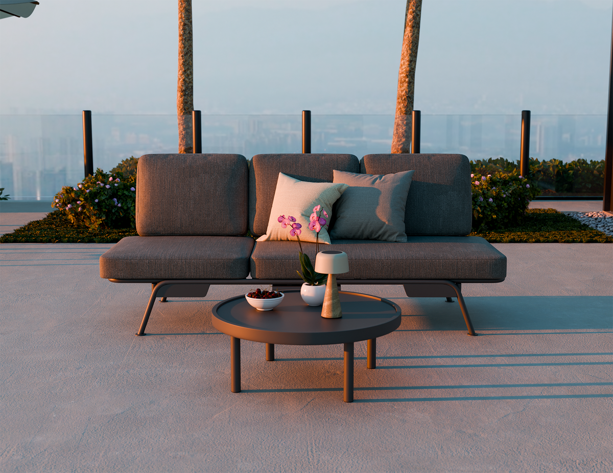 Gray outdoor sofa with cushions and a small table on a patio with palm trees in the background.