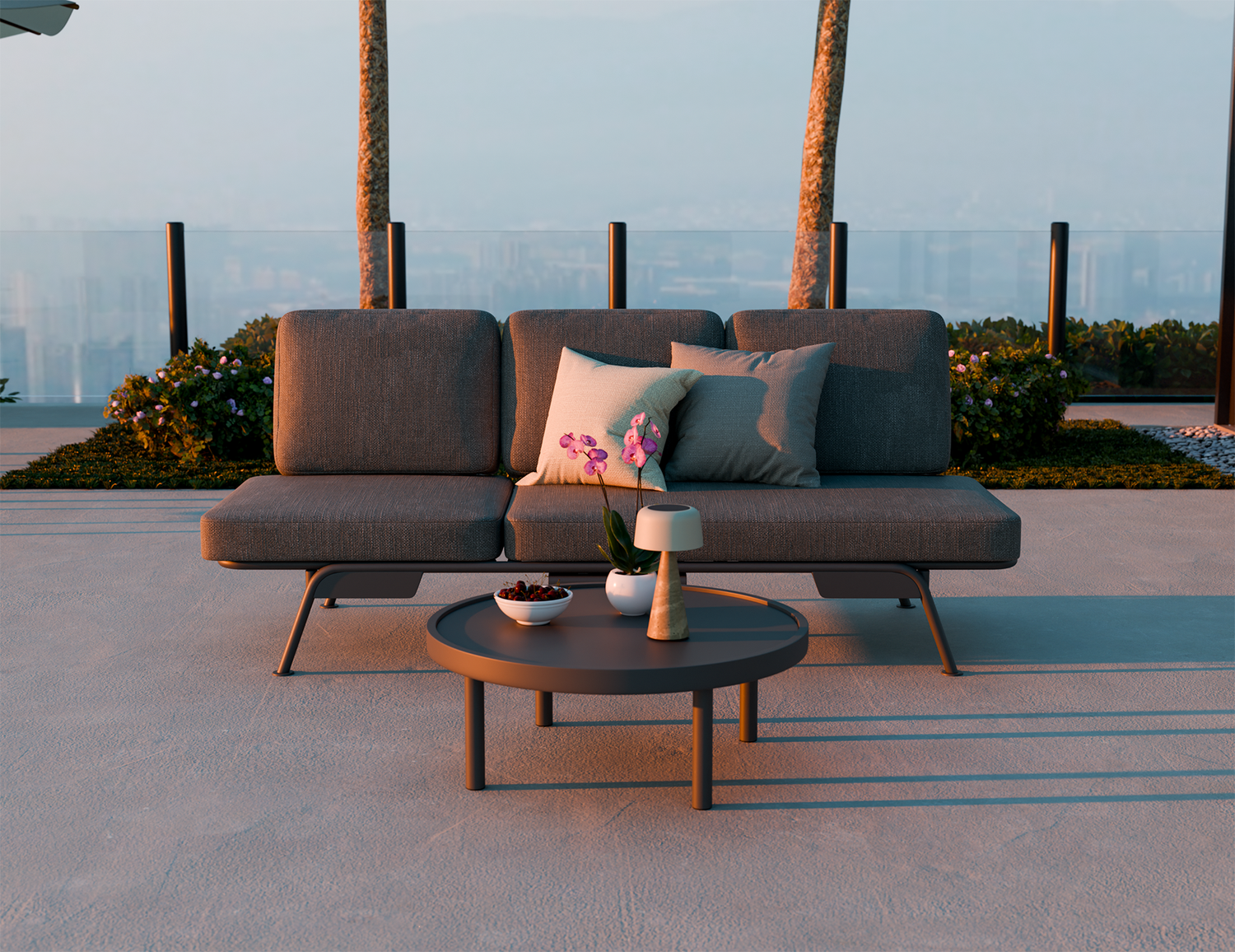 Gray outdoor sofa with cushions and a small table on a patio with palm trees in the background.