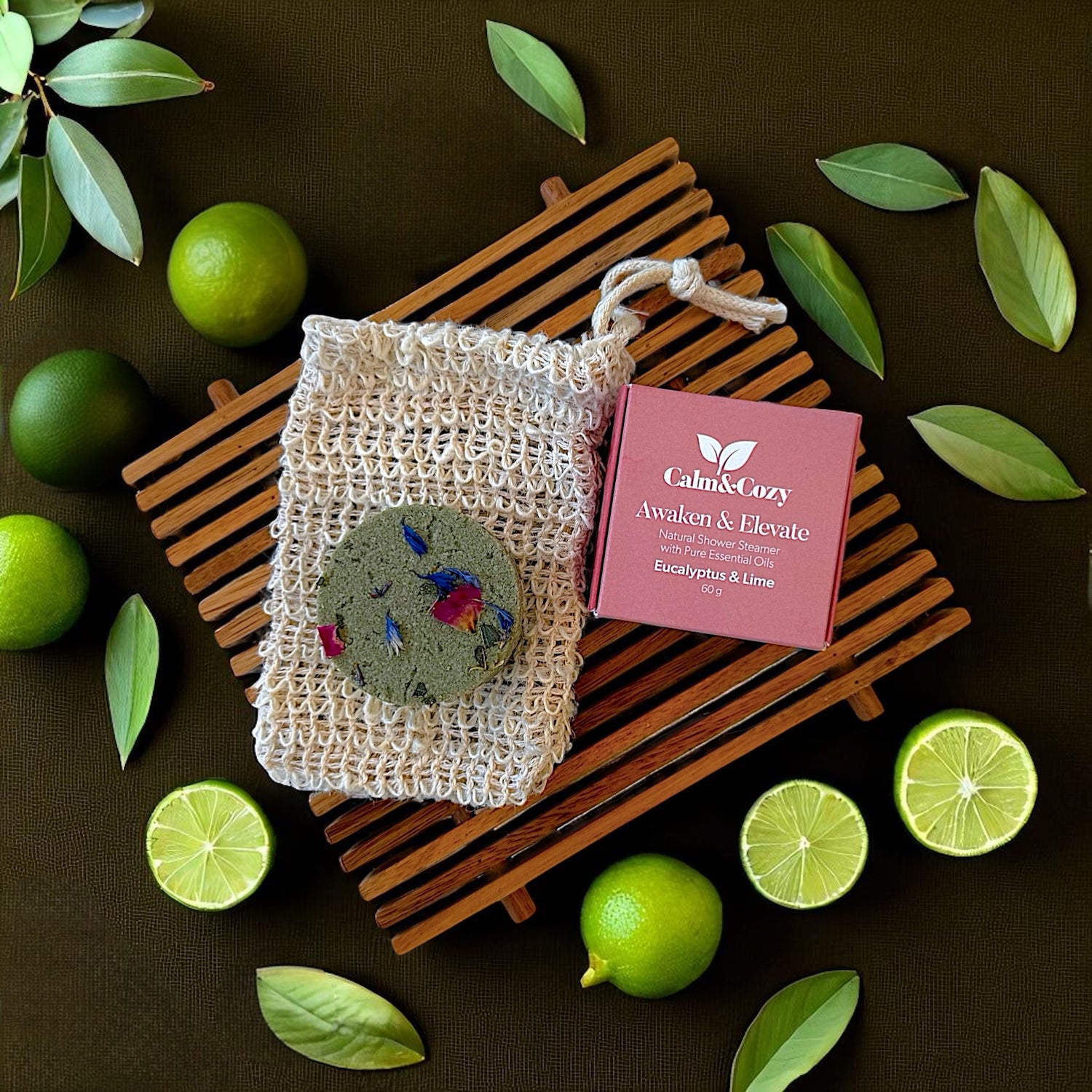 Calm & Cozy soap in a mesh bag with packaging on a dark surface with limes and leaves.