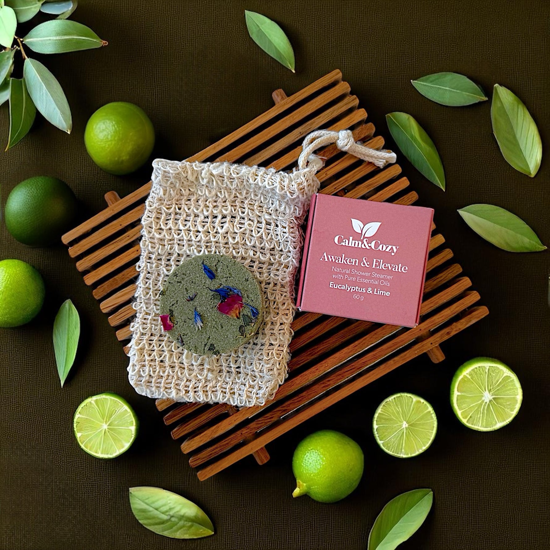 Calm & Cozy soap in a mesh bag with packaging on a dark surface with limes and leaves.