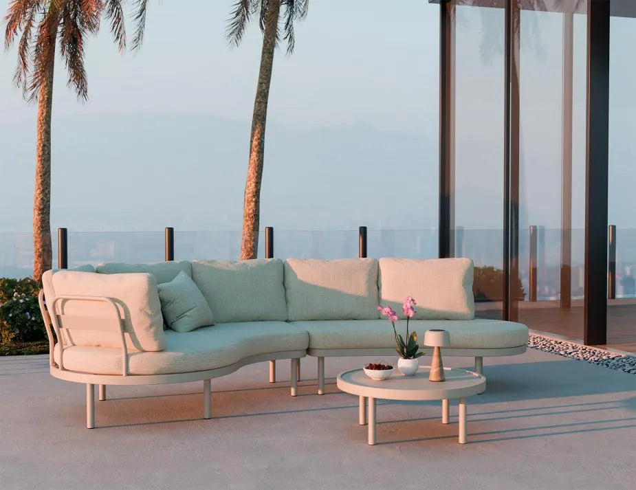 Outdoor patio set with sectional sofa and coffee table on a deck with palm trees and ocean view.