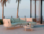 Outdoor patio set with sectional sofa and coffee table on a deck with palm trees and ocean view.