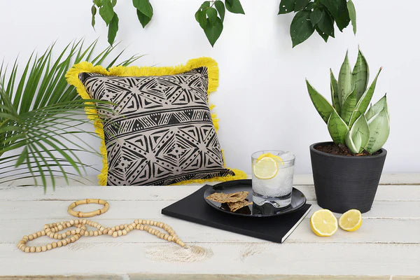 Decorative pillow with geometric pattern on a table with plants and a glass of water.