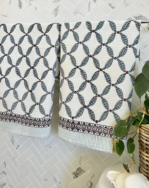 Pair of patterned towels hanging on a rack against a tiled wall.