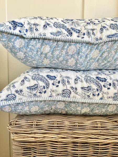 Two floral-patterned pillows stacked on a wicker basket against a light wooden panel background.