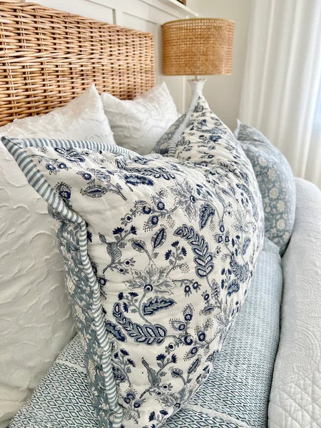 Floral-patterned throw blanket draped over a sofa with a wicker headboard and lamp in the background.