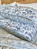 Stack of patterned fabric pieces on a bed with wicker headboard