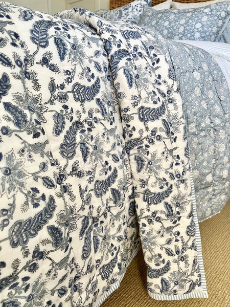 Floral patterned quilt draped over a bed with a textured surface.