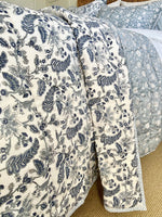 Floral patterned quilt draped over a bed with a textured surface.