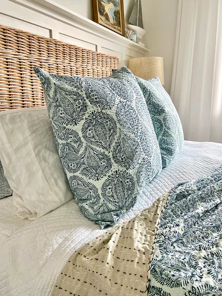 Patterned pillows and blanket on a bed with a wicker headboard.
