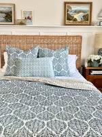 Bedroom with wicker headboard, patterned bedding, and framed artwork on the wall.