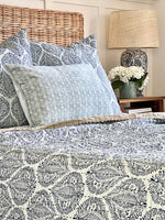 Bed with patterned bedding, pillows, and a lamp in a bedroom setting.